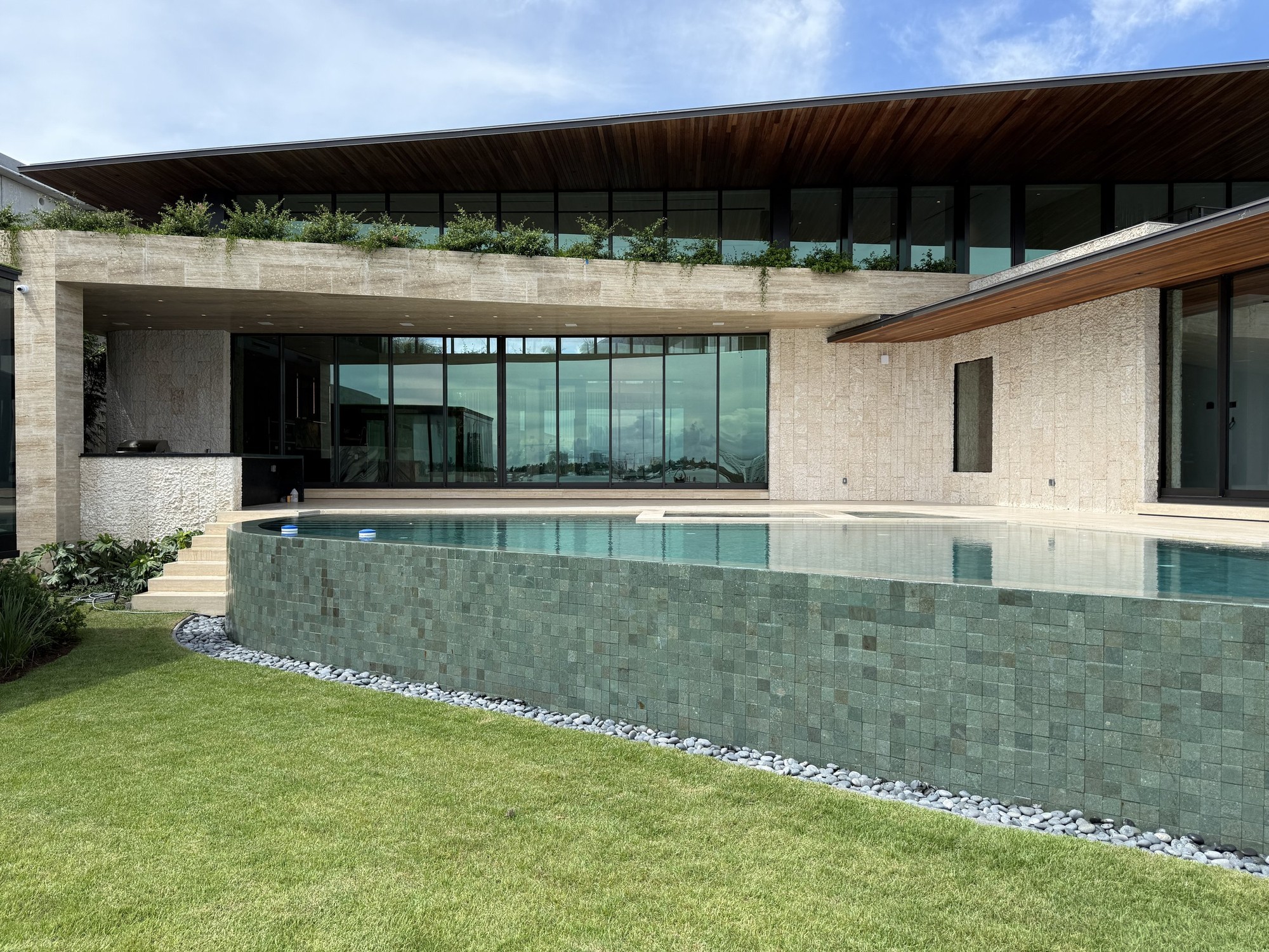 Contemporary residence with a curved pool wall, stone facade and lawn